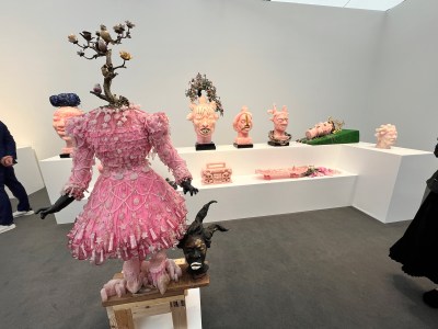 A fair booth with a child's dress that sprouts a tree-like plant. In the background are sculpted heads in shades of pink.