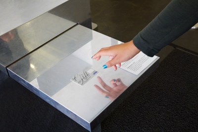 A hand with blue nail polish hovers above a gift credit card lying on reflective metal surface.