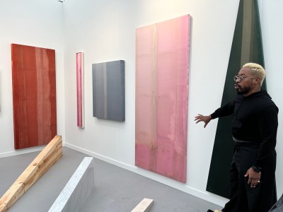 A Black man standing amid abstract paintings and sculptures.