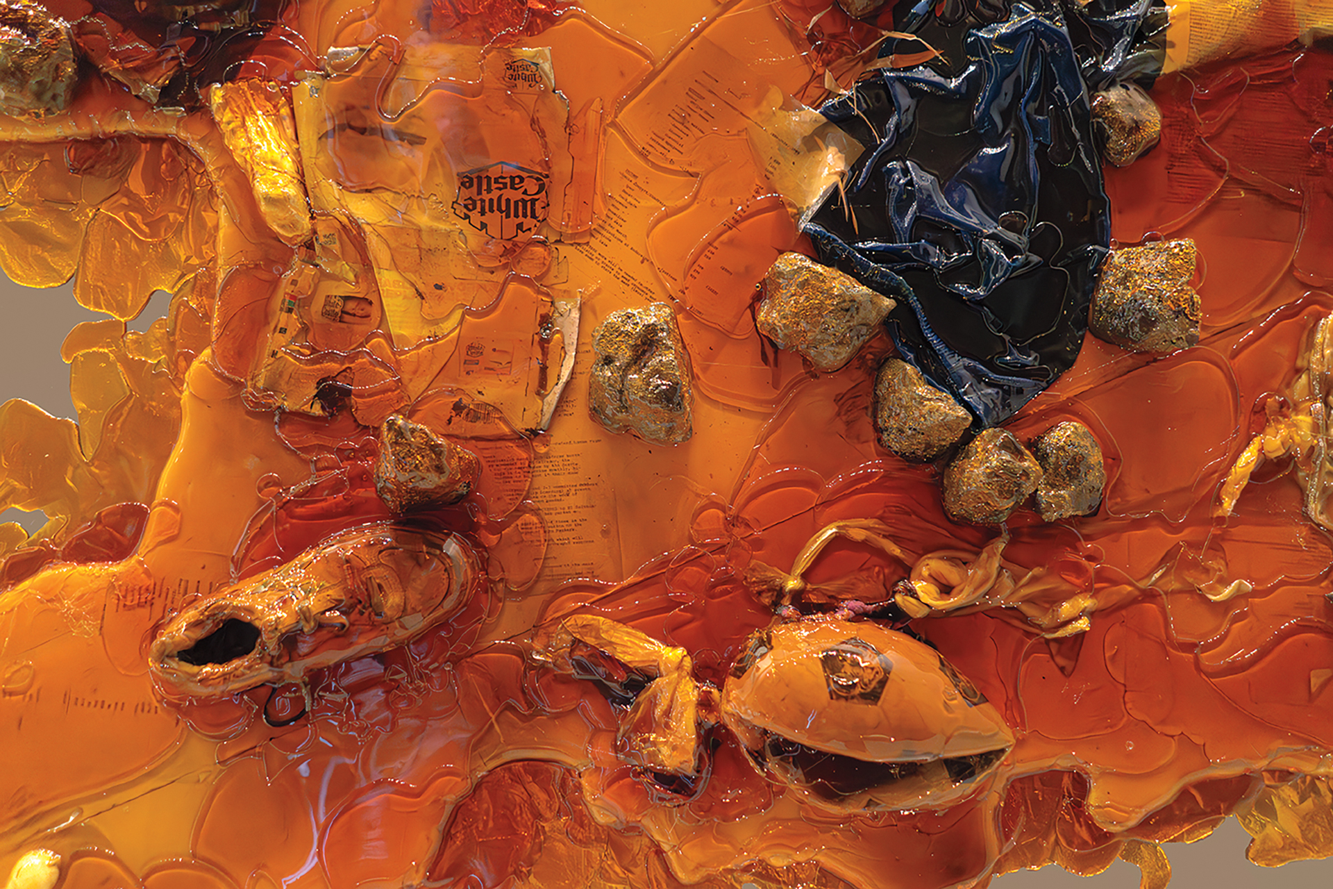 Detail of a floorpiece made from various objects, like clothing, shoes, rocks, paper that have been covered with amber that has hardened.