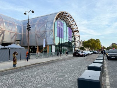 The entrance to a large, nearly circular convention center building with several cars in front.