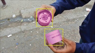 Two olive skinned hands hold canisters; one is labeled "triple-chaser" and both are highlighted in pink and with yellow boxes by machine vision.
