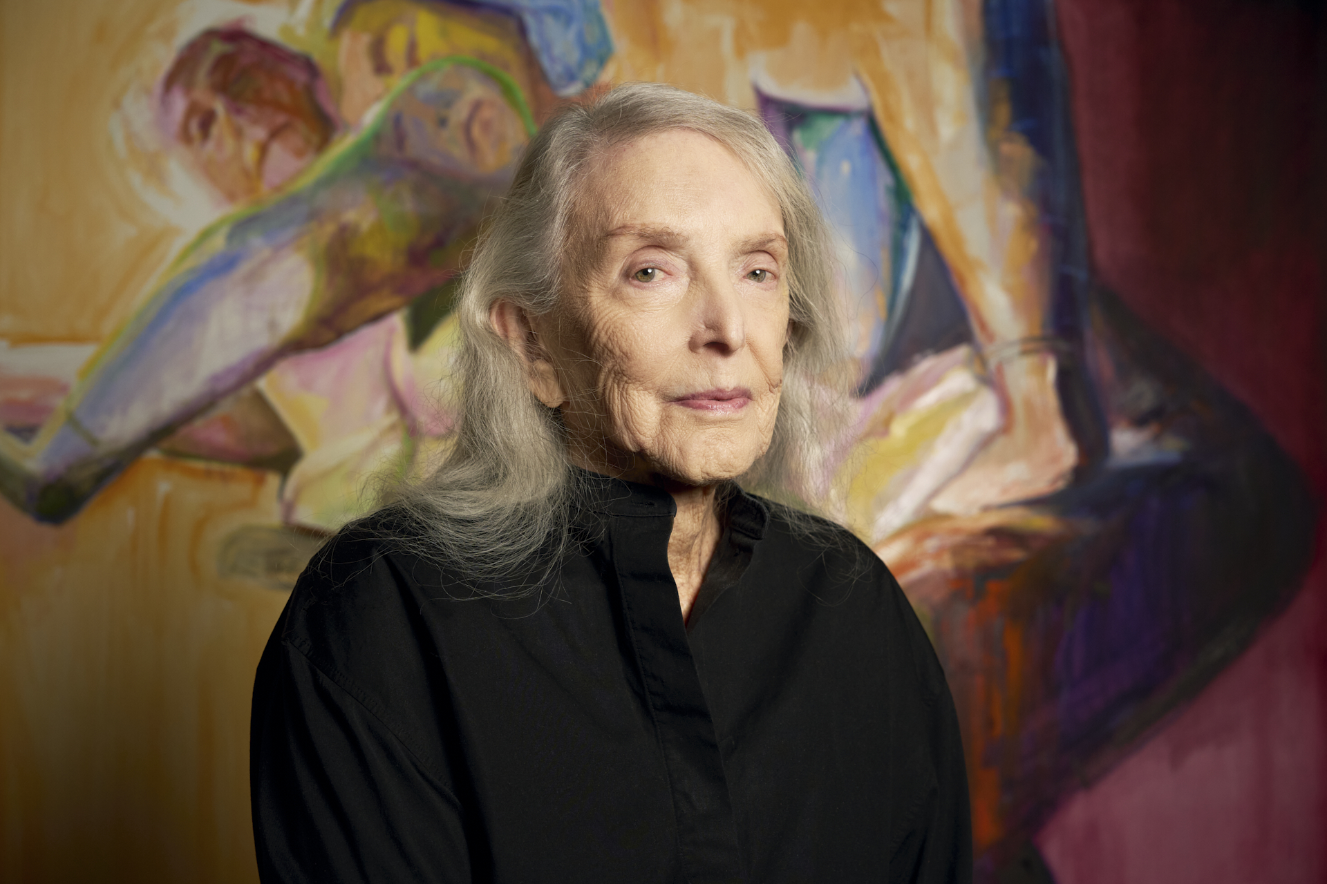 A 90-something white woman with beautiful silver hair and blue eyes is seen in front of an expresive, colorful, double self-portrait that she painted.
