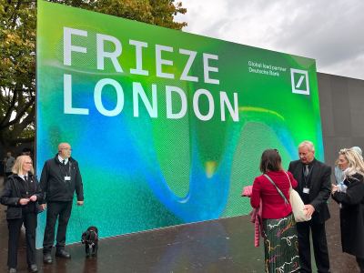 People stand before a large sign reading FRIEZE LONDON.