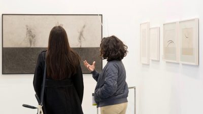 Two women look at a painting hanging on a wall at the India Art Fair.