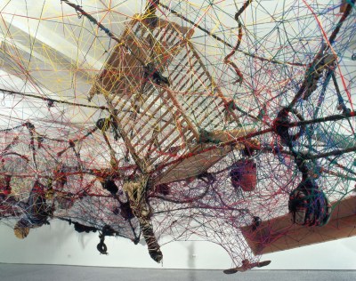 A cradle strung up with multihued thread. The assemblage also ensnares many other unidentifiable objects.